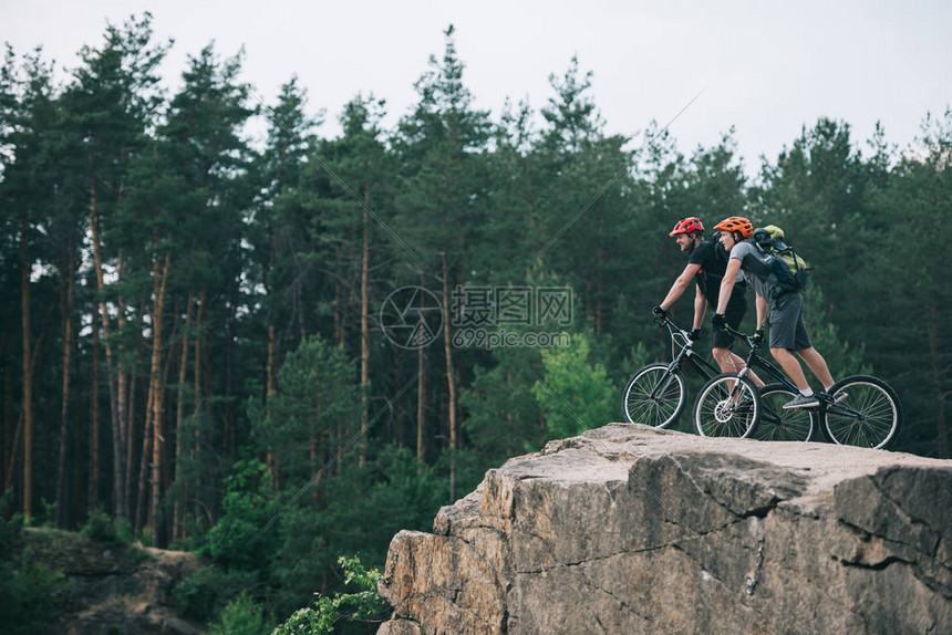 在森林中岩石悬崖上骑着山地自行车的防护头盔上的男极端骑自图片