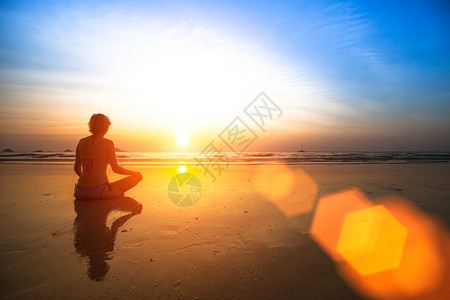 日落时坐在海边的瑜伽女人图片