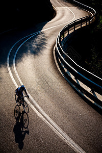 一名男骑自行车的人骑着公路自行车沿着铺好的山路骑行背图片