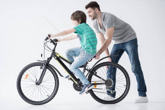 父亲帮助儿子骑白色自行图片