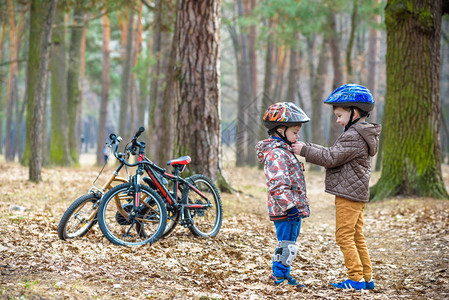 两兄弟准备在春季或秋季森林公园骑自行车帮助兄弟姐妹戴头盔的大孩子安全和保护概念快乐的男孩最好的朋友在一图片