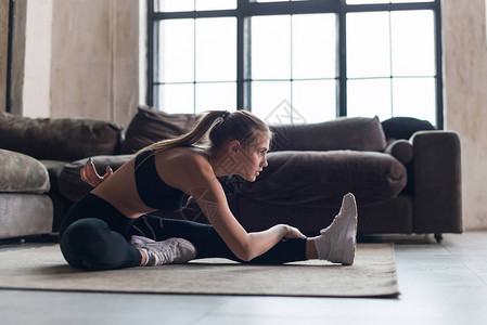 在运动前穿运动服肌肉变暖的滑雪女运动员在家里地板上做伸展练习图片