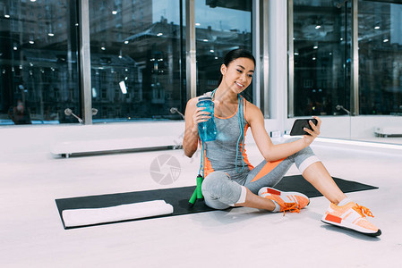 微笑的亚洲女运动员坐在健身垫上图片
