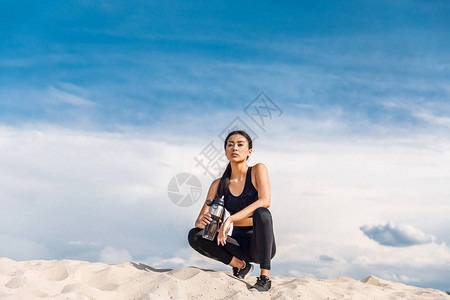 身着运动瓶子的疲累女运动员躺在沙滩图片