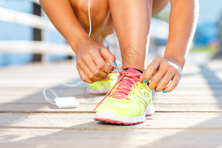 跑鞋系鞋带的女人夏末或秋季女健身跑步者准备在海滨户图片