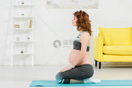 坐在客厅健身垫子上的运动服孕妇图片