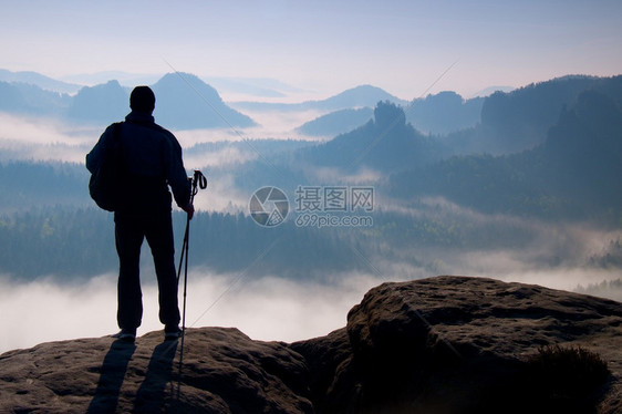 手拿着杆的游客的剪影阳光明媚的春天破晓在落基山脉背着背包的徒步旅行者站在迷雾笼罩的山谷上方的图片