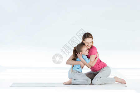 快乐的母亲和女儿坐在瑜伽垫上拥抱着欢乐图片