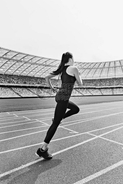 参加运动服的年轻健身女子在赛道体育场上跑图片