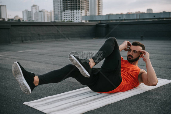 英俊的运动员在屋顶的瑜伽垫上做仰卧起坐图片
