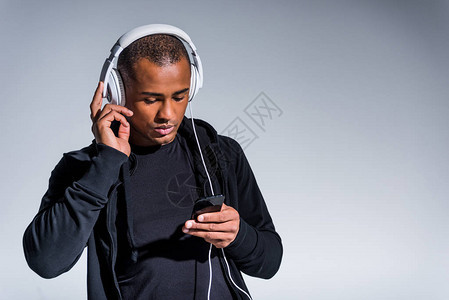 手持耳机的非洲年轻英俊青年男子使用在灰色上隔图片