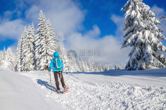 穿着蓝下外套背包穿雪鞋和木棍在冬季山区风景中行走的年图片