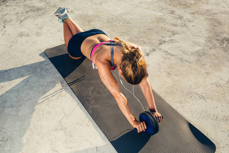 听耳机中运动女运动员在健身垫上用滚盘锻炼图片