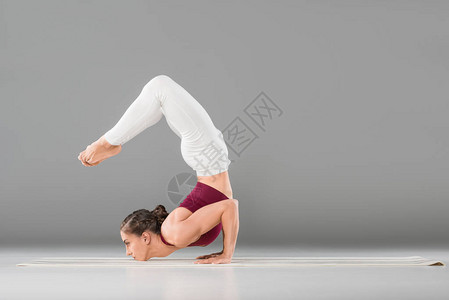 年轻女子用弯曲的腿姿势表演瑜伽倒立的侧视图图片