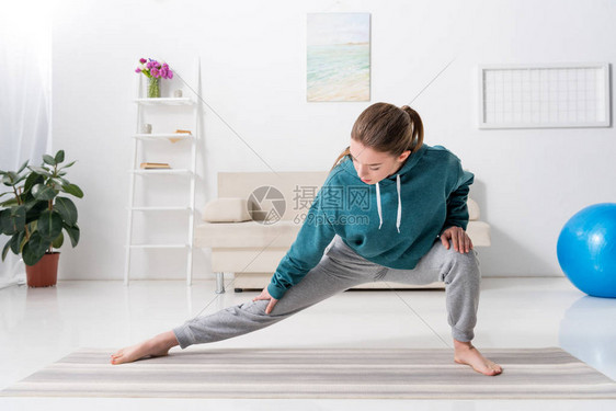 在家瑜伽垫上伸展双腿的女孩图片