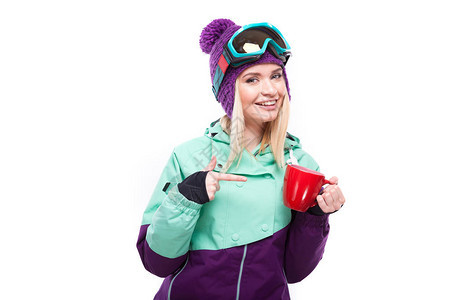 身穿紫色滑雪服和滑雪护目镜手放在脸上看着相机拿着红杯指着杯子的图片