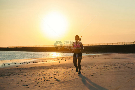 拥有智能手机的女运动员在沙滩上与阳光抗日跑步时使用臂图片