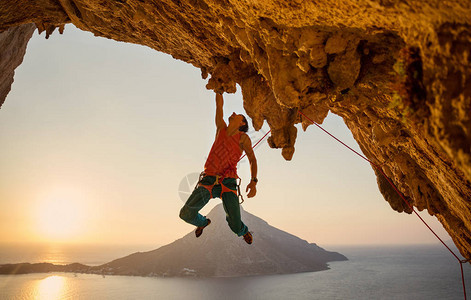 男攀岩者一只手挂在日落时悬崖上图片