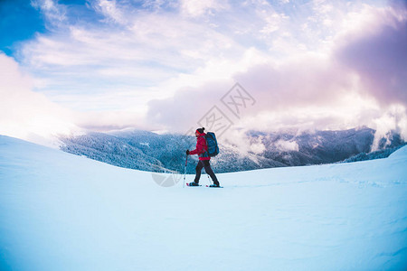 一个穿着雪鞋和登山杖的人在山上冬季旅行攀登一个登山者反对美丽的天空与云彩积极的生活方式图片