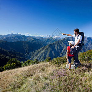 在山的暑假父亲和年幼的儿子站在高山草甸上男人指了一个方向图片