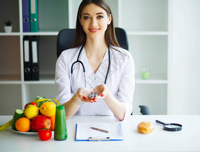 健康营养师医生带着美丽的笑容医生坐在桌边的灯室里新鲜水果和蔬菜健康饮图片