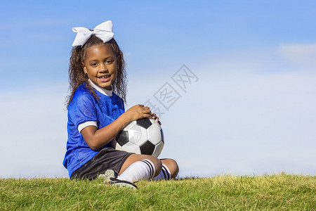 一个可爱年轻的非洲裔美国女足球运动员拿着球坐在草地上图片