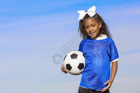 一个可爱年轻的非洲裔美国女足球运动员拿着一个球站在草地上图片