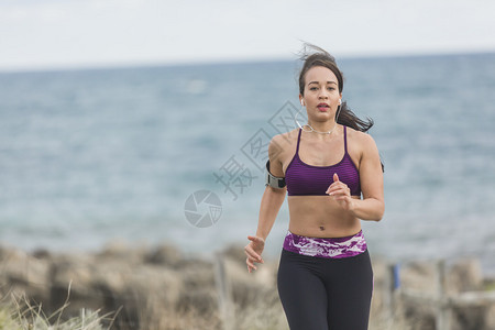 健身图片身穿健身服的年轻运动女运动员在寒冬多云的海滩边背景