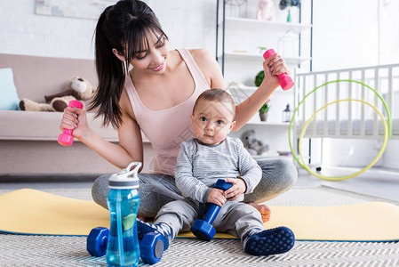 年幼健康的母亲在家与孩子一起坐在瑜伽垫子上做运图片