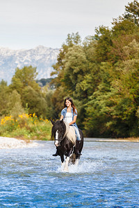年轻女骑马青年在山地上穿越蓝色河图片