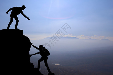 团队的朋友徒步旅行帮助彼此信任中的援助剪影徒步者在登山队顶上互相帮背景图片