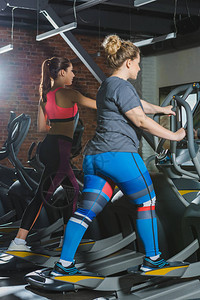 在健身房的跑步机上训练的运动型和超重女图片