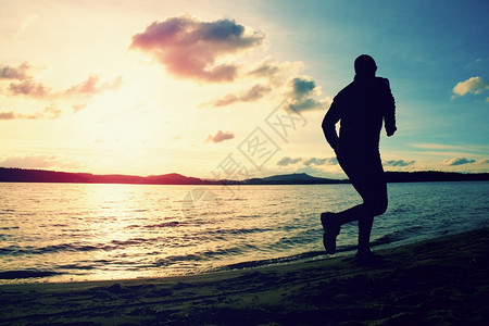 高个子运动员沿着日出的海岸奔跑图片