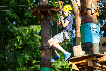 快乐可爱穿蓝T恤和头盔的男孩在冒险公园玩耍玩耍拉绳子爬上木楼梯图片