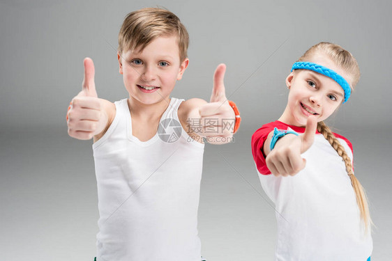 在运动服中笑可爱的男女儿童展示在灰色儿童体育概念上图片