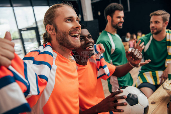 身穿橙色T恤和围巾的多元文化足球迷兴奋地用球庆祝胜利图片