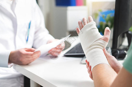 受伤的病人在医院办公室或急诊室用绷带展示医生的手腕和手臂骨折手部扭伤应力骨折或重复劳损护士帮背景图片