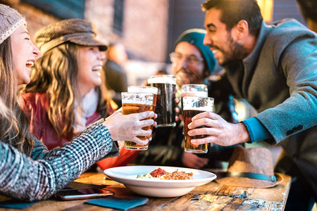 友好的家伙在冬天的时候在户外的啤酒厂吧接近快乐的女孩与年轻人一起喝醉的友谊概念在欢乐时光促销时一起喝啤酒图片