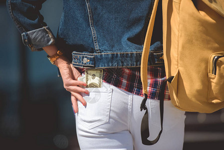 在牛仔裤口袋装背包和美元钞票的现代女旅图片