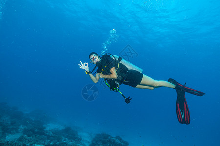 探索海底的年轻女子水肺潜水员显示好的迹象与美丽的岩石和珊图片