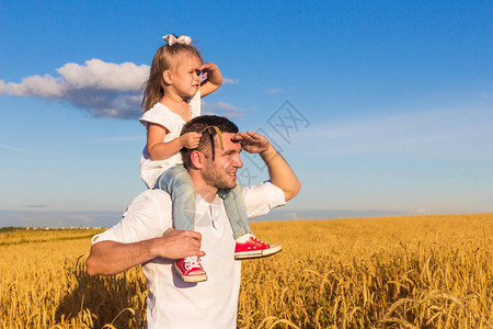 爸带着一个坐在他肩膀上的小女儿站在麦田中央图片