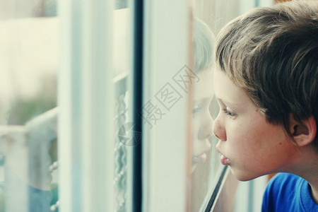 可爱的6岁男孩透过窗户看图片