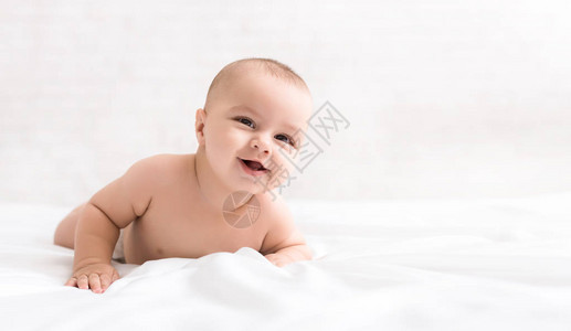 可爱的微笑婴儿爬在房间里的床图片