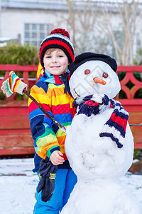 有趣的孩子男孩穿着五颜六色的衣服堆雪人图片