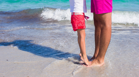 在白沙滩上小女孩站在她父亲的脚下图片