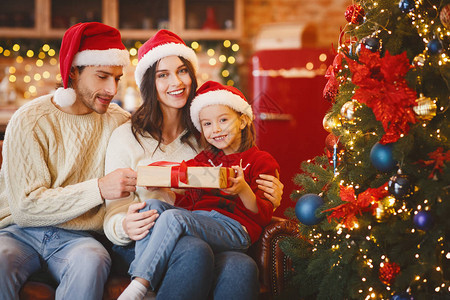 带着圣诞礼物的快乐小女孩在家和父母一起庆祝圣诞晚会图片