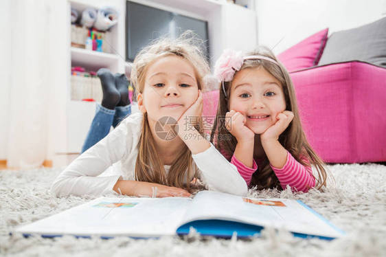 两个快乐的小女孩读书躺在家里地板上图片