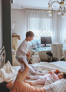快乐的男孩在一个轻松的早晨与家人一起跳上床和在床上玩耍的肖像图片