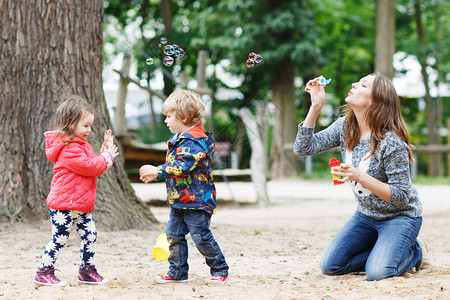 快乐的母亲和两个小孩在夏天的操场玩肥皂泡游图片