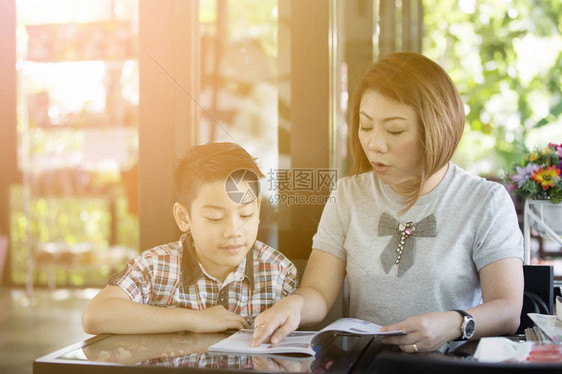 亚裔母亲在客厅与儿子一起阅读一本带微笑的书和阳图片